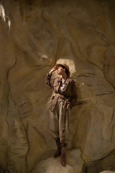 Comprimento total de arqueólogo em roupas estilo safari olhando para longe perto da rocha no deserto — Fotografia de Stock