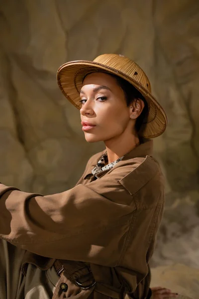 Jolie archéologue en veste marron et chapeau safari regardant caméra dans le désert — Photo de stock