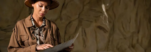 Jeune archéologue en veste beige pointant vers l'ancienne carte dans le désert, bannière — Photo de stock