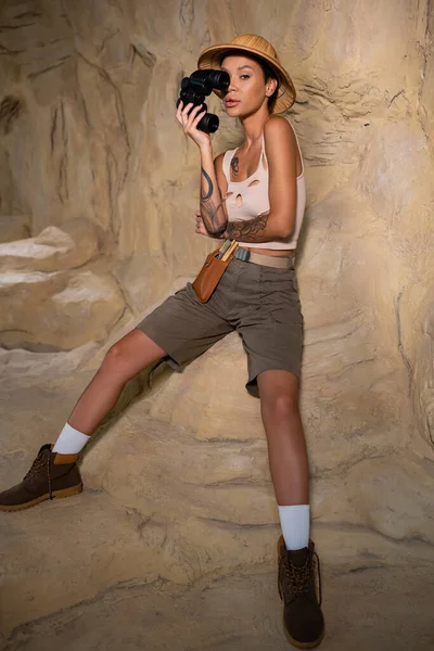 Full length of sexy archaeologist in shorts and tank top holding binoculars near face — Stock Photo