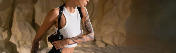 Partial view of tattooed archaeologist with gun in holster, banner — Stock Photo