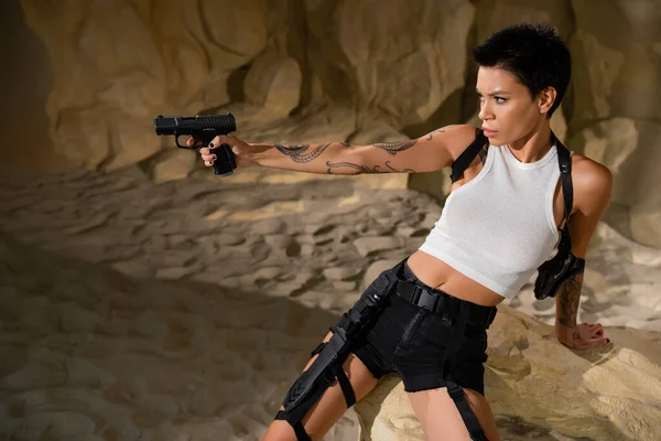 Concentrated archaeologist with handgun in outstretched hand near rock in cave — Stock Photo