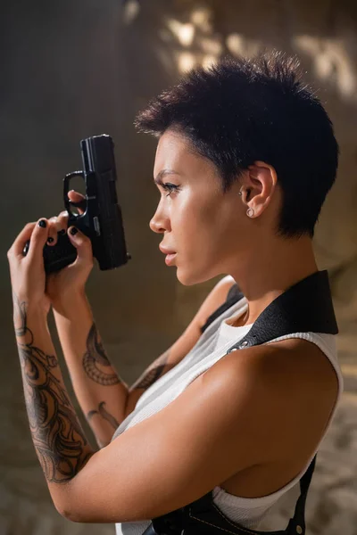 Side view of brunette and tattooed archaeologist holding handgun in desert — Stock Photo
