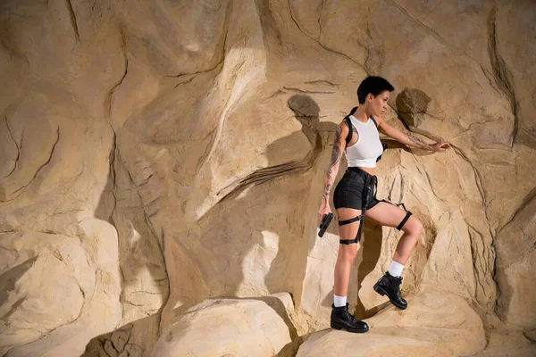 Junge Archäologin mit Waffe bewaffnet steht in Höhle in der Nähe von Felsen — Stockfoto