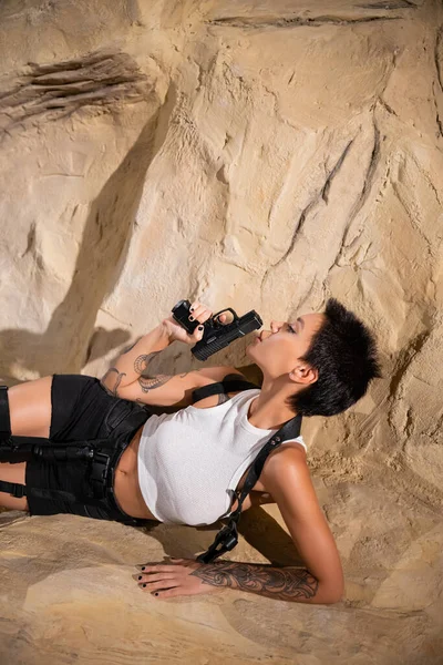 Sexy morena arqueólogo soplando a pistola mientras está acostado en cueva - foto de stock