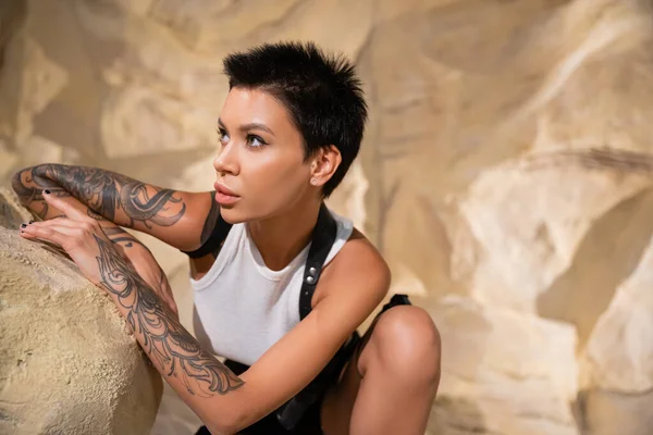 Брюнетка с татуировкой археолог смотрит в сторону, прячась за камнем в пустыне — стоковое фото