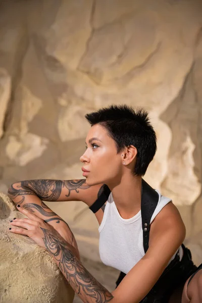 Vista lateral del arqueólogo tatuado con el pelo corto mirando hacia otro lado en la cueva - foto de stock