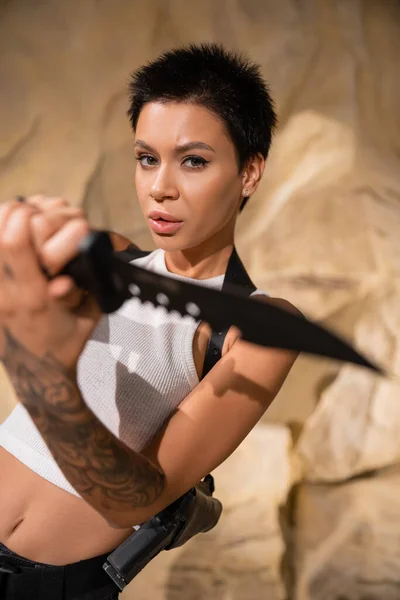 Tattooed and sexy archaeologist with short hair holding knife on blurred foreground — Stock Photo