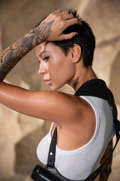 Pretty and sexy archaeologist with tattoo adjusting short hair — Stock Photo