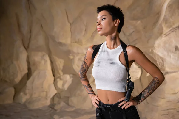 Armed and tattooed archaeologist with dirty crop top standing with hands on hips — Stock Photo