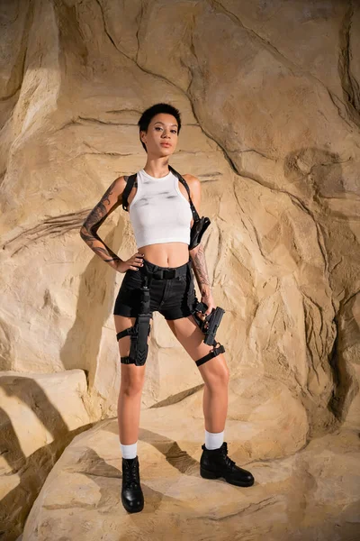 In voller Länge bewaffneter Archäologe im sexy Outfit, der mit der Hand auf hüfthohen Felsen steht — Stockfoto