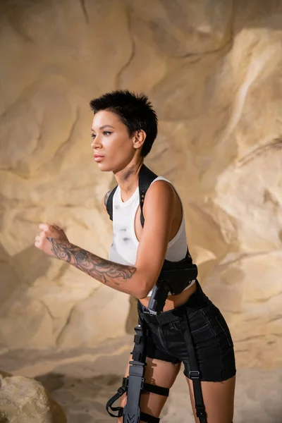 Archéologue armé et tatoué en tenue sexy courir dans la grotte — Photo de stock