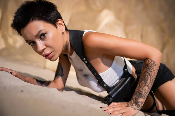 Sexy e tatuato archeologo in abiti sporchi e fondina strisciare sulla sabbia in grotta — Foto stock
