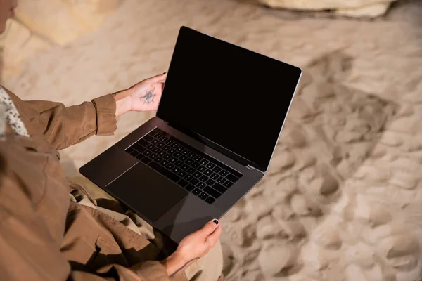 Cropped view of archaeologist with tattoo using laptop in cave during expedition — Stock Photo