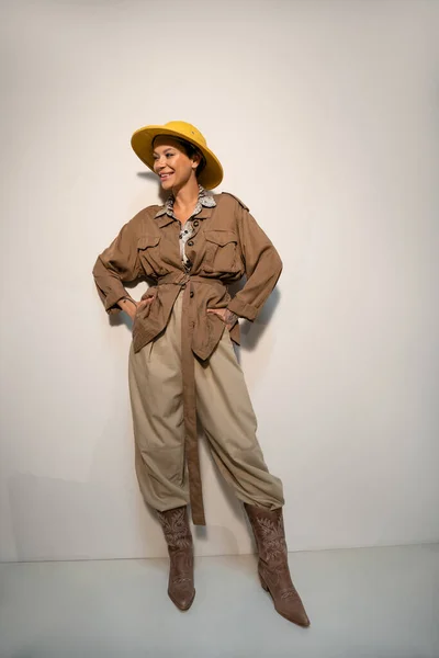 Pleine longueur de heureux archéologue en chapeau safari et veste beige posant avec les mains dans les poches sur gris — Photo de stock
