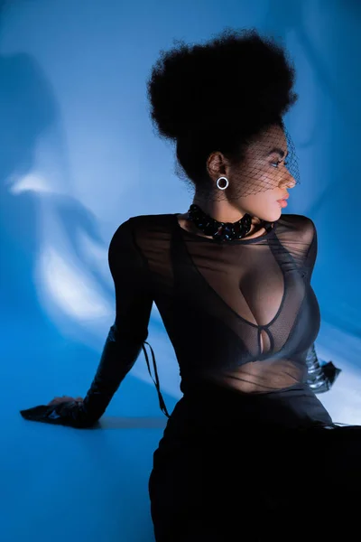 Ricci donna afroamericana in camicia trasparente e velo nero in posa su blu — Foto stock