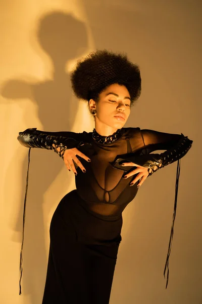 Modelo afroamericano de moda en sexy camisa transparente y sujetador negro posando en amarillo - foto de stock