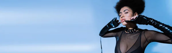 Jeune femme afro-américaine en chemise à manches longues transparente noire et voile regardant la caméra sur bleu, bannière — Photo de stock
