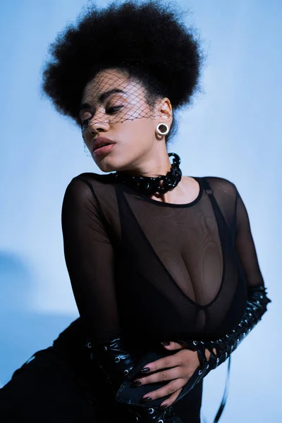 Jeune femme afro-américaine en tenue sexy et voile noir posant sur bleu — Photo de stock