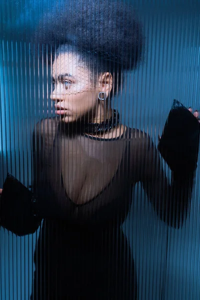 Jeune femme américaine africaine en tenue sexy et voile noir regardant loin derrière le verre froissé — Photo de stock