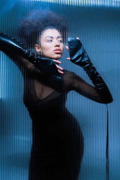 Молодая африканская американка в черной вуали и сексуальной одежде, смотрящая сквозь потрепанное стекло — стоковое фото