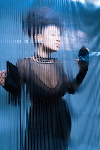 Красива афро-американська модель в чорному сексуальному вбранні, дивлячись далеко, торкаючись скрученого скла — стокове фото