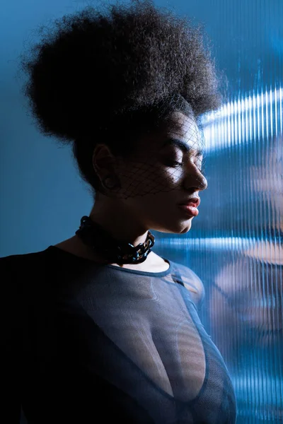 Jeune femme américaine africaine en tenue sexy et voile noir près de verre froissé avec éclairage bleu — Photo de stock