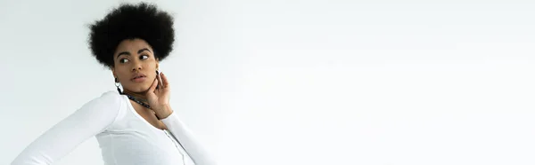 Bella donna afro-americana toccare viso pulito mentre guardando lontano isolato su bianco, banner — Foto stock