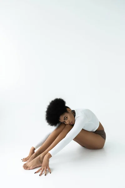 Full length of young african american woman in long sleeve shirt and panties sitting on white — Stock Photo