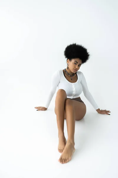 Young african american woman in long sleeve shirt and panties sitting on white — Stock Photo