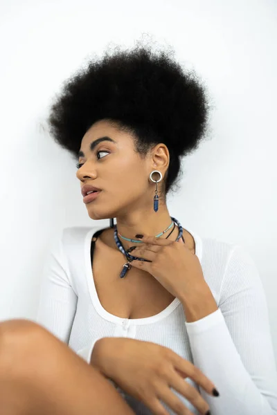 Mujer joven afroamericana con pelo rizado ajustando collares aislados en blanco - foto de stock
