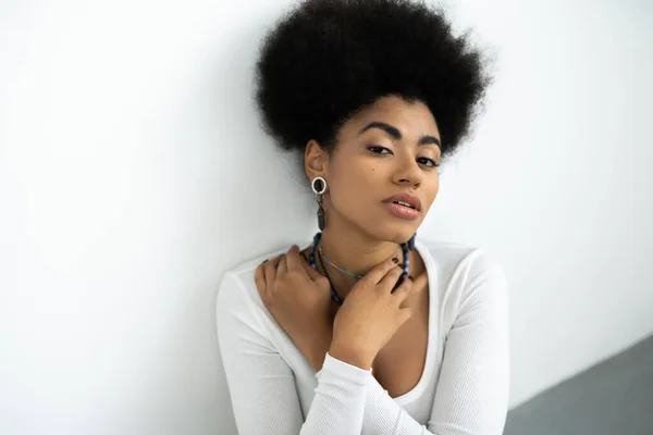 Mulher americana africana bonita com cabelo encaracolado ajustando colares em branco e cinza — Fotografia de Stock