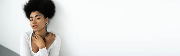 Jolie femme afro-américaine aux cheveux bouclés ajustant les colliers sur blanc et gris, bannière — Photo de stock