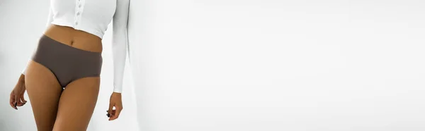 Vista ritagliata della donna afroamericana in camicia a maniche lunghe e biancheria intima in piedi vicino al muro bianco, banner — Foto stock