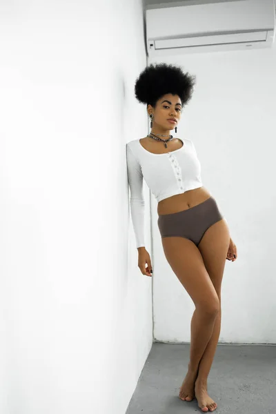 Full length of barefoot african american woman in long sleeve shirt and underwear standing near white wall — Stock Photo