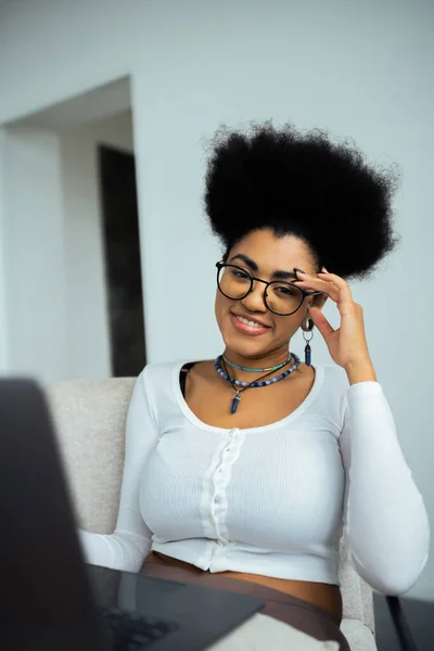 Freelancer afro-americano feliz em óculos sorrindo perto de laptop em casa — Fotografia de Stock