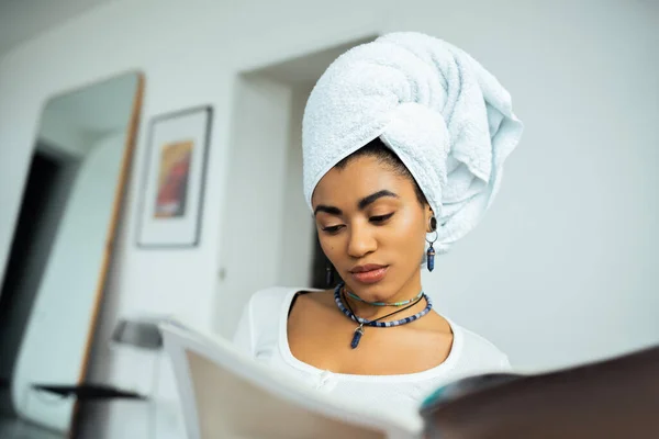 Young african american woman with towel on head reading magazine — Stock Photo