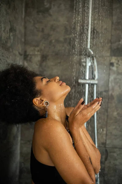 Pleased african american woman with closed eyes taking shower at home — Stock Photo