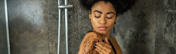 Jeune femme afro-américaine massant le corps avec gommage dans la cabine de douche, bannière — Photo de stock