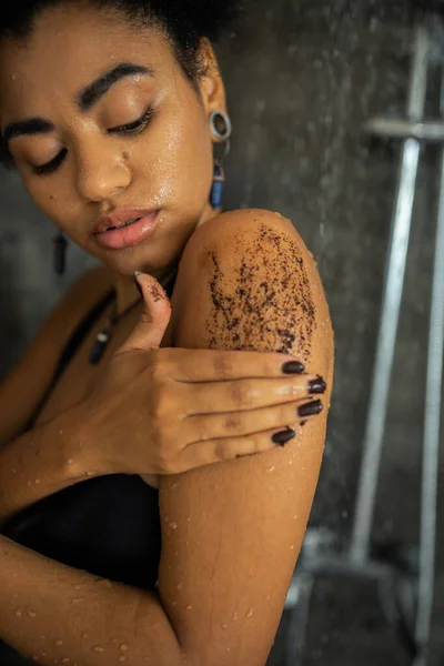 Joven afroamericana americana aplicando exfoliante natural en hombro en ducha - foto de stock