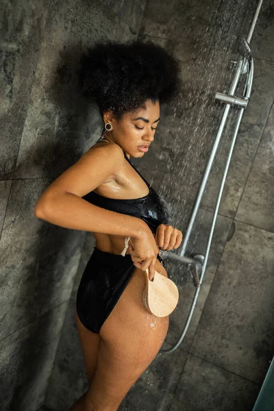 Bouclé afro-américaine femme massant la hanche avec brosse dans la douche — Photo de stock