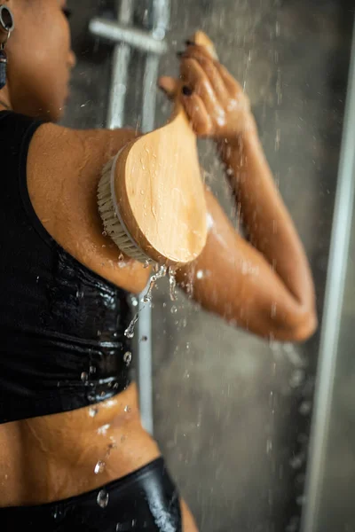Vista laterale della donna afroamericana massaggiante indietro con pennello in doccia — Foto stock