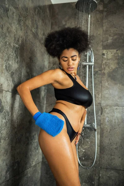 Curly Africano americano mulher limpeza corpo com luva de massagem no chuveiro cabine — Fotografia de Stock