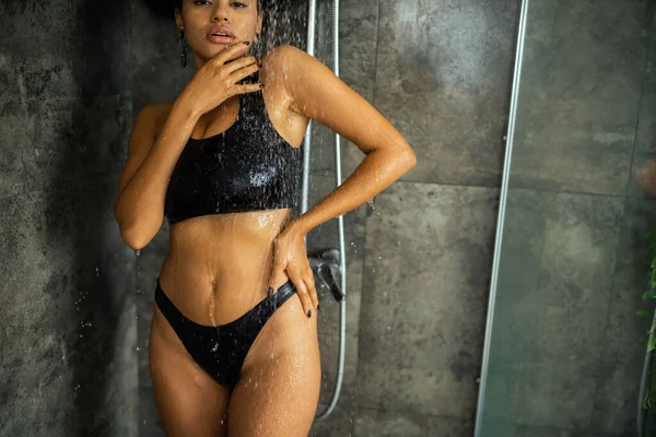 Vue recadrée de la femme afro-américaine en haut de la culture et culotte prenant douche et regardant la caméra à la maison — Photo de stock