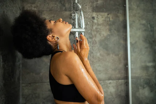 Vue latérale de la jeune femme afro-américaine en haut de culture prenant une douche à la maison — Photo de stock