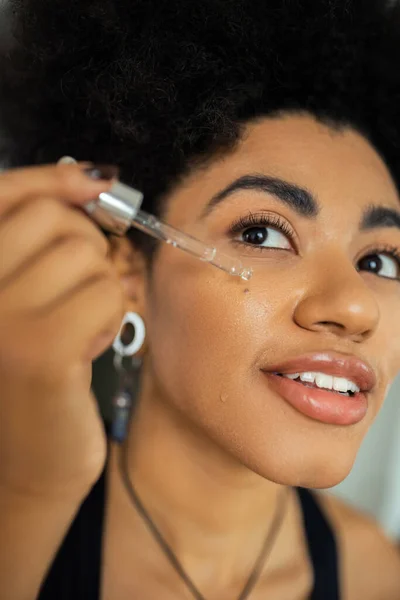 Young african american woman applying serum on cheek at home — Stock Photo