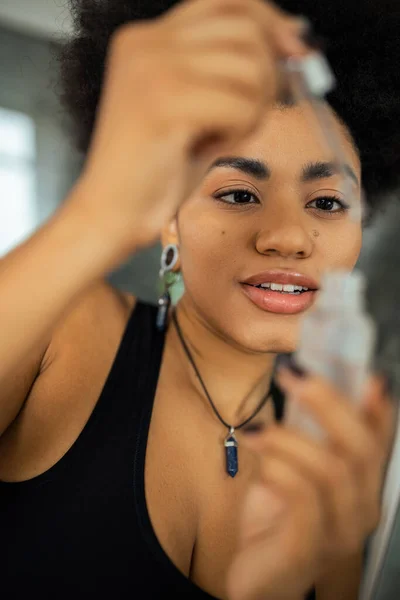 Mujer afroamericana joven sosteniendo suero borroso y gotero en el baño - foto de stock