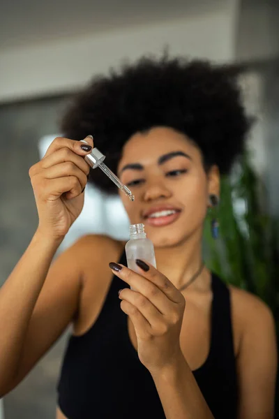 Blurred african american woman holding dropper and serum at home — Stock Photo