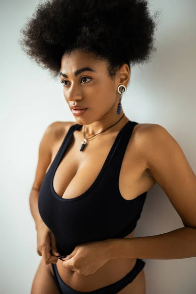 Curly african american woman in crop top and panties looking away while standing near wall — Stock Photo