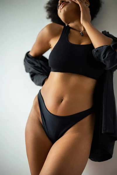 Vue recadrée de la jeune femme afro-américaine en chemise noire et sous-vêtements debout près du mur — Photo de stock